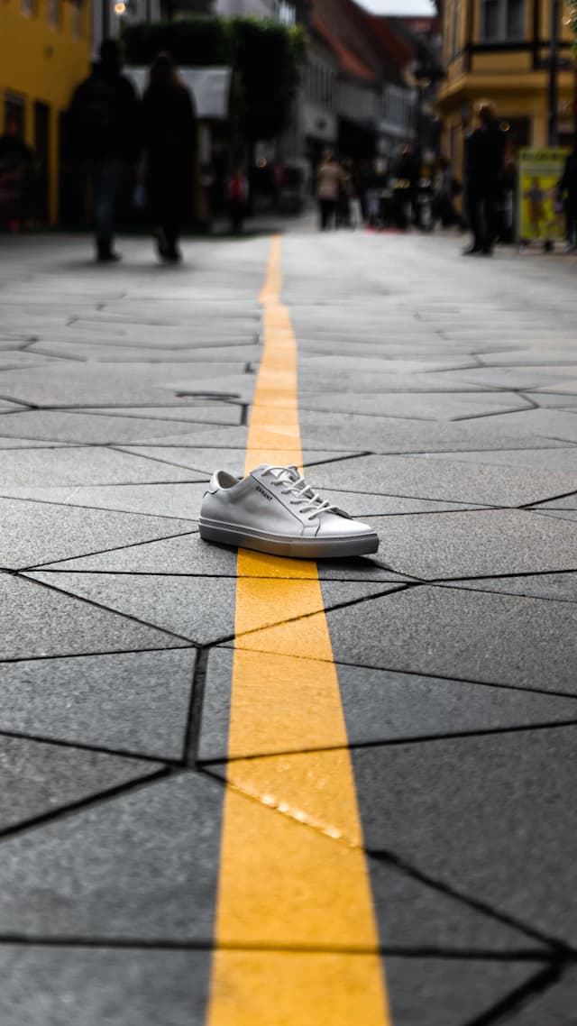 A white running shoe on a city sidewalk, low angle, clean light